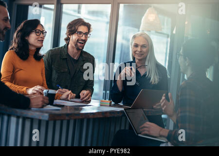 Felice gruppo di persone aventi una riunione in ufficio. Giovane uomo ridendo durante l incontro con i colleghi di lavoro in piedi intorno a. Foto Stock