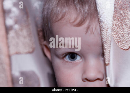 Un ragazzino gioca nascondere dietro una tenda. Foto Stock