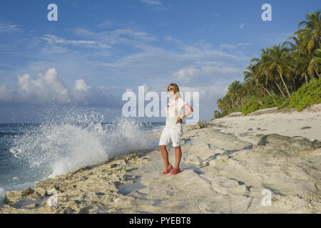 Giovane donna in abiti estivi in piedi su una spiaggia e guardando all'orizzonte su un'esotica isola tropicale Foto Stock