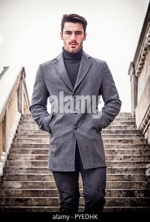Bello barbuto giovane uomo outdoor in inverno moda, vestita di nero turtleneck maglione di lana e blazer giacca in impostazione della città Foto Stock