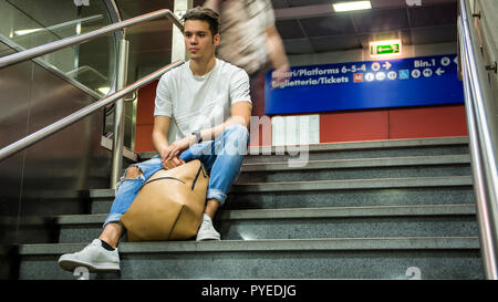 Bel giovane uomo seduto sulle scale' gradini di marmo, zaino accanto a lui Foto Stock