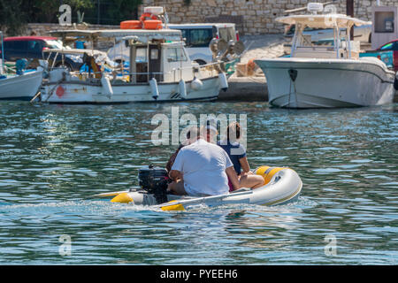 Tre persone in un piccolo gommone o gara nel porto di Kassiopi sull'isola greca di Corfù Foto Stock