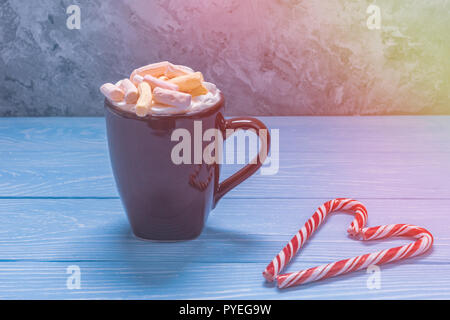 Tazza marrone con bevanda calda e marshmallows su un tavolo di legno accanto alla quale sono dolci di Natale Foto Stock