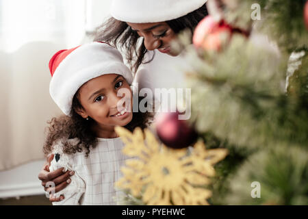 Felice famiglia americana africana in santa claus cappelli decorare albero di Natale insieme a casa Foto Stock