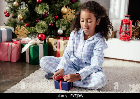 Adorable African American bambino in pigiama apertura regalo di Natale a casa Foto Stock