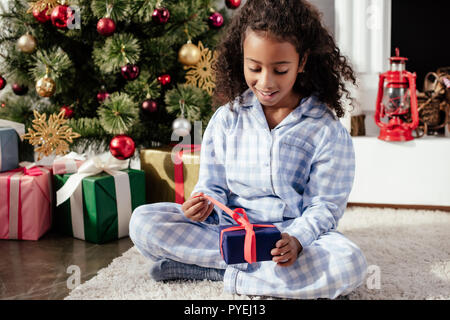 Emozionato adorabili african american bambino in pigiama apertura regalo di Natale a casa Foto Stock