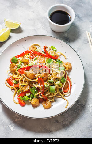 Friggere le tagliatelle con verdure e gamberi su sfondo di calcestruzzo. Foto Stock