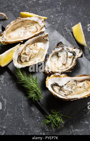 Aprire le ostriche con il limone su pietra scura sullo sfondo di texture Foto Stock