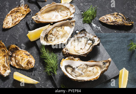 Aprire le ostriche con il limone su pietra scura sullo sfondo di texture Foto Stock