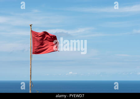 Bandiera rossa sventolata su un palo. Le nuvole e la vista del mare sullo sfondo. Visualizzazione orizzontale Foto Stock