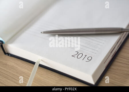 Anno Nuovo 2019 office organizer Calendario, smartphone, bicchieri e sliver penna a sfera sulla scrivania in legno. Immagine con copia spazio. Messa a fuoco selettiva. Foto Stock