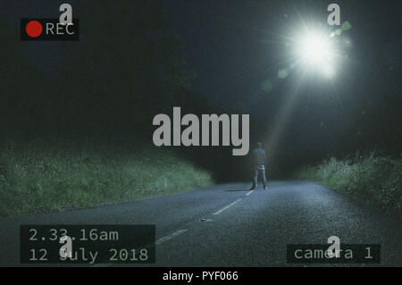 Una solitaria figura in piedi in strada di notte mentre guardando un UFO e il fascio di luce nel cielo Foto Stock