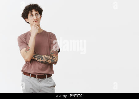 Per essere o che non è questione. Riflessivo artistiche e creative smart curly-haired guy in bicchieri con i baffi e raffreddare i tatuaggi sui bracci sfrega mento guardando in alto pensiero, mentre dipinge piano in mente Foto Stock
