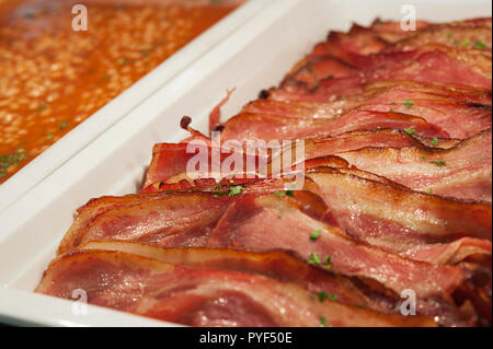 Closeup shot di vassoi di fette di bacon arrosto e fagioli al forno, sana colazione cucinata opzioni, l'aggiunta di proteine e fibra per una dieta Foto Stock