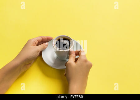Elevato angolo di donna mani tazza da caffè su sfondo giallo stile minimalista. Appartamento laico, vista dall'alto isolato. Foto Stock