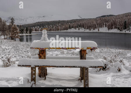 Poco carino pupazzo di neve dalla prima neve su un tavolo contro lo sfondo di un lago, montagne e alberi dorate in autunno Foto Stock