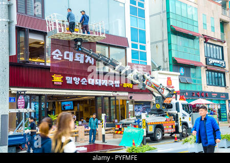 Operai utilizzare una gru per sollevare in posizione e di abete un nuovo frontalino all'esterno di un ristorante di Haeundae, Busa, Corea del Sud. Foto Stock