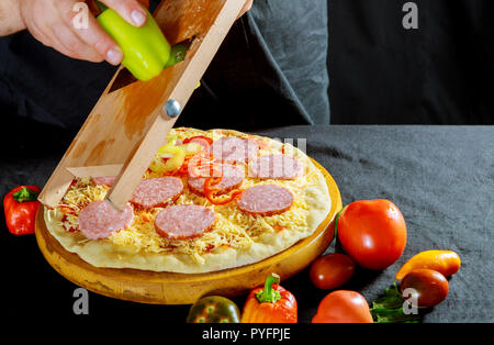 Pizza con impasto crudo per affettare un peperone verde con ingredienti e pepe per pizza. La cucina italiana tradizionale. Foto Stock