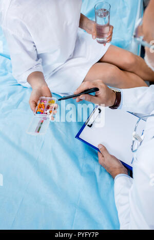 Immagine ritagliata di mezza età medico maschio con uno stetoscopio oltre il collo rivolto a pillole per il paziente di sesso femminile nella stanza di ospedale Foto Stock