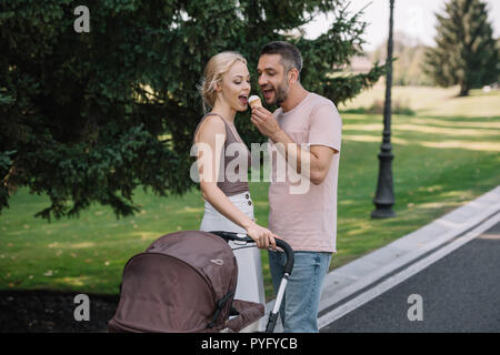 Marito moglie di alimentazione con gelato nelle vicinanze baby carrello in posizione di parcheggio Foto Stock