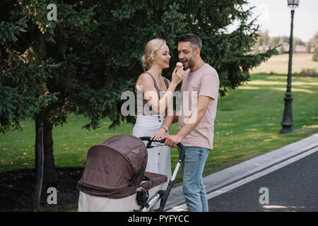 Moglie marito di alimentazione con gelato nelle vicinanze baby carrello in posizione di parcheggio Foto Stock