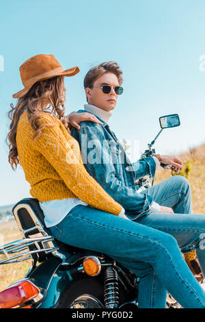Coppia giovane seduto sulla moto e rilassarsi sul prato rurale Foto Stock
