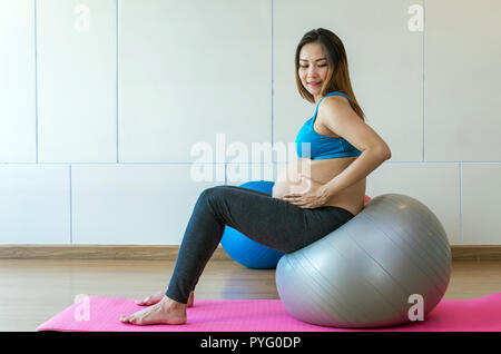 Ritratto di asian femmine gravide di fare esercizio nella sala sportiva, seduto sulla grande palla, sana maternità concept Foto Stock