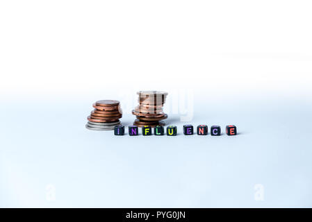 Pila di monete e testo influenza, realizzata con piccoli blocchi su sfondo bianco Foto Stock