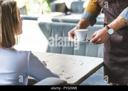 Ritagliato colpo di cameriere che serve tazza di cappuccino per client femmina presso il cafe Foto Stock
