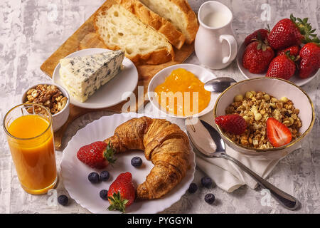 Sana colazione con latte in una piccola jur, granola, fragola, dadi, formaggio, succhi di frutta, marmellate, croissant, su sfondo bianco laici piatta Foto Stock