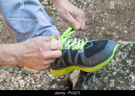 Mani maschio occupare lacci delle scarpe su un acceso sneaker, vicino. Parte di sportivo sneakers di legatura. Gamba su una roccia. Uomini sportswear, del piede atleta, Foto Stock