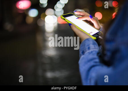 Ragazza puntare il dito sullo schermo smart phone su sfondo bokeh luce nella notte città atmosferica, Foto Stock