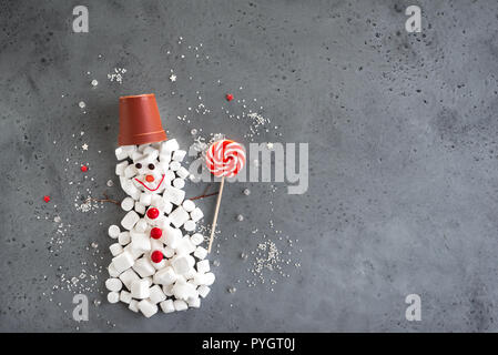 Dolce natalizio pupazzo di neve. Composizione di natale con il rosso e bianco dolci di stagione in forma di uomo di neve su grigio, copia dello spazio. Natale biglietto di auguri, c Foto Stock