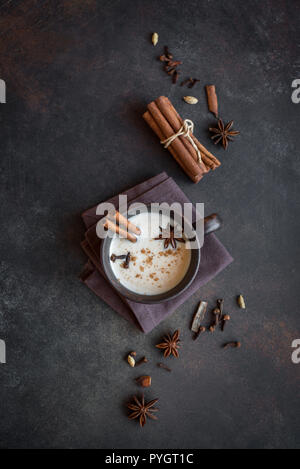 Tradizionale indiano Masala chai tè in tazza di ceramica con ingredienti. Spicy tè nero con latte rustico sfondo scuro, copia dello spazio. Foto Stock
