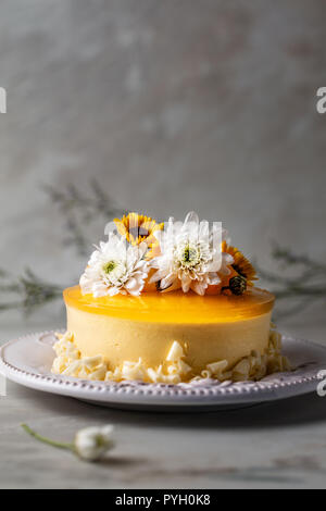 Mango cheesecake con gelatina di giallo topping, di fiori e di mango fresco pezzi su sfondo grigio , composizione verticale Foto Stock