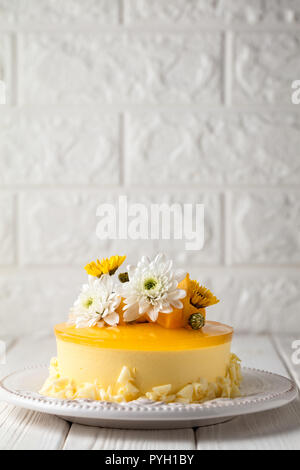 Mango cheesecake con gelatina di giallo topping, di fiori e di mango fresco pezzi su sfondo bianco, composizione verticale Foto Stock