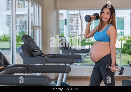 Ritratto di asian femmine gravide di fare esercizio nella sala sportiva, sollevamento pesi, sana maternità concept Foto Stock