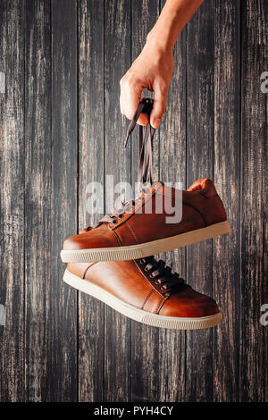 Mano trattiene per lacci in cuoio marrone scarpe da uomo su sfondo scuro Foto Stock