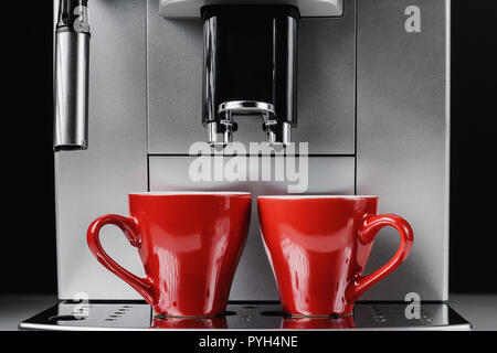 Moderno e macchina per il caffè e due bicchieri rossi a sfondo nero, close up Foto Stock