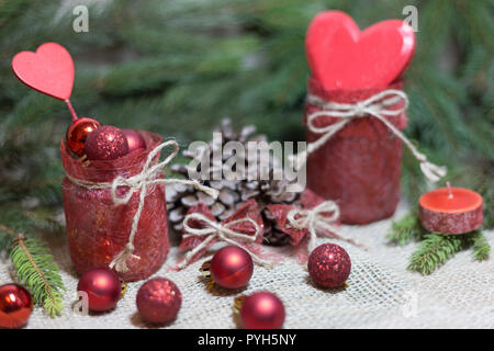 Rosso di ornamenti, cuori, candela e pigne sull'annata sullo sfondo di Natale Foto Stock