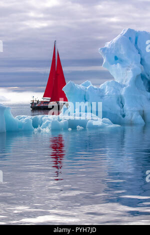 Bella rossa di barca a vela in artico accanto a un enorme iceberg che mostra la scala. Ilulissat Tourist Nature, Disko Bay, la Groenlandia. Foto Stock