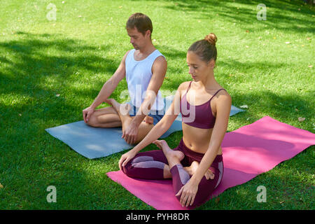 A piena lunghezza shot di coppia giovane seduto nel parco e meditando insieme mentre fare yoga insieme. Foto Stock