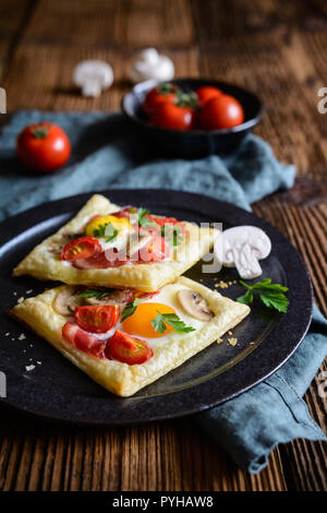 Gustosa pasta sfoglia torte con uova, bacon, funghi e pomodoro Foto Stock