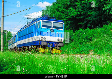 Un blu locomotiva elettrica passando la campagna ceca. Un treno che corre attraverso la valle verde. Il trasporto ferroviario in Repubblica Ceca Foto Stock