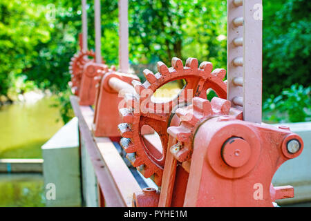 Close-up di un rosso metal gear su la paratoia 7. Meccanismo per aprire la diga. Vecchia ruota dentata sul fiume. Trasferimento all'apertura della diga. Vecchio cogw Foto Stock