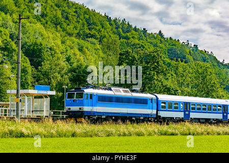 Un blu locomotiva elettrica passando la campagna ceca. Un treno che corre attraverso la valle verde. Il trasporto ferroviario in Repubblica Ceca. Una giornata di sole Foto Stock