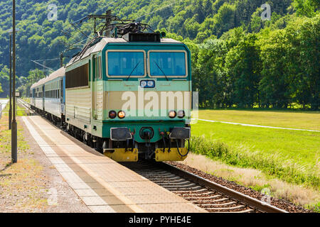 Un verde locomotiva elettrica passando la campagna ceca. Un treno che corre attraverso la valle verde. Il trasporto ferroviario in Repubblica Ceca. Una giornata di sole Foto Stock