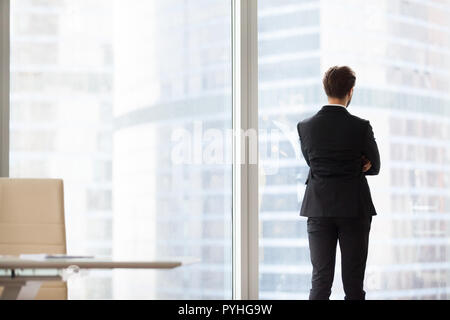 Vista posteriore ritratto di imprenditore di successo in piedi da una finestra Foto Stock