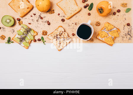 Composizione alimentare sano panini con persimmon, kiwi, banana, chia e i dadi per la prima colazione su bianco tavolo in legno, vista dall'alto. Piatto telaio laici per dolci Foto Stock