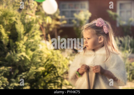 Bella carino bambino ragazza principessa nel mantello esterno ritratto con luce calda del sole soft verde giardino formale il concetto di sfondo felice royal infanzia li Foto Stock